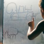 child drawing in window condensation with finger